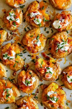 Super crispy smashed potatoes topped with sour cream, bacon and chives, resting in an oven pan.